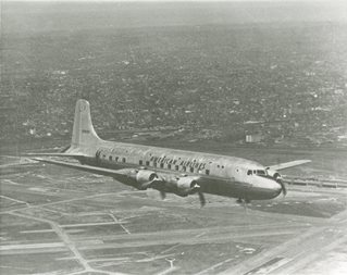 Early model of a passenger airplane flying low over farmland.