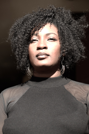 Headshot of a woman with black curly hair wearing a black dress.