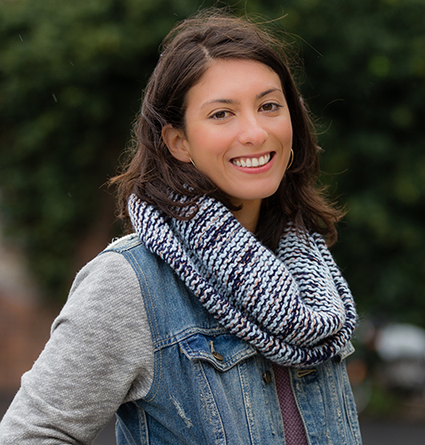 Headshot of a woman with dark brown hair, a denim jacket, and a blue scarf smiling.