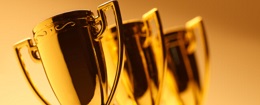 Three gold trophies in a row against a yellow background.