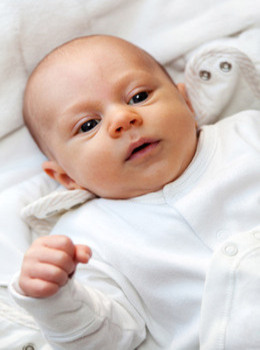 Baby laying down in a white onesie.