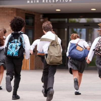 Four boys wearing backpacks walk towards a school.