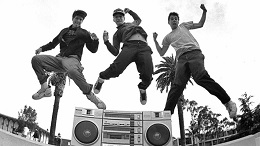 Three young men jump in the air in front of a boom box.