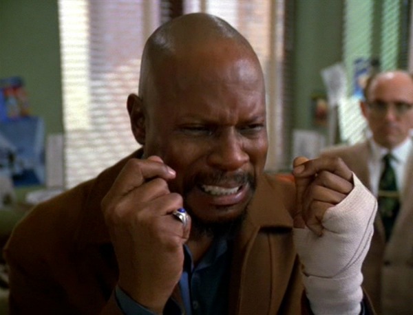 Film sill of a man with a bald head wearing a tan jacket and a pinky ring.