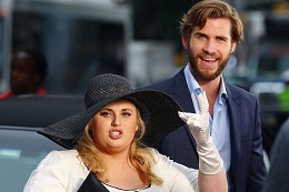 Man in blue suit and a woman in a white dress with a large black hat.