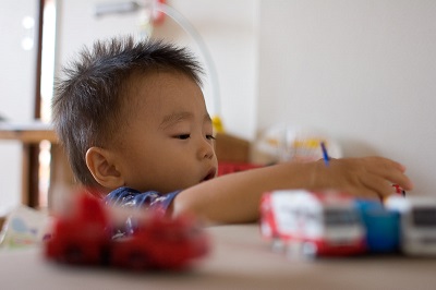 Young boy reaching for toy cars on a tabletop.