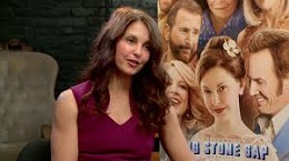 Woman with long brown hair and a maroon shirt sits in front of a movie poster for Big Stone Gap.