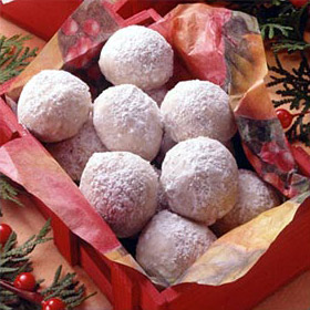 White spherical cookies covered in powdered sugar are stacked up in tissue paper in a box as a Christmas gift.