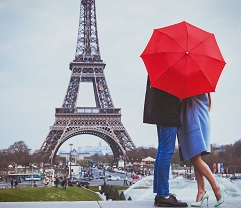 Couple embracing under a red umbrella near the Eiffel Tower in Paris.