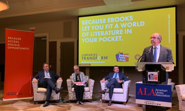 A man speaks at a podium during an American Library Association event, with three panelists seated before a yellow screen about ebooks.