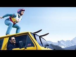 A person in ski gear balances on the roof of a moving yellow car in a snowy mountain setting, while a driver looks on from inside.