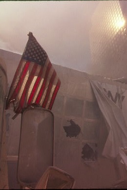An American flag hangs from a pile of rubble.