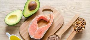 Overhead shot of an avocado, a salmon filet, and spoons filled with nuts and seeds.