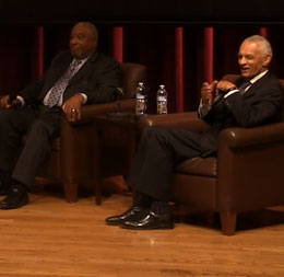 Two men sitting on auditorium stage.