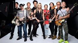 A group portrait of a large band posing with their guitars and basses against a bright white studio background.