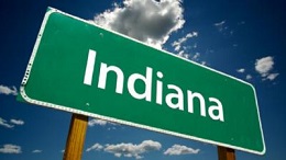 Green road sign that reads Indiana against a blue sky.