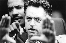 Black and white close-up of two men; the man in the foreground frames a shot with his hands while the man behind him looks on intently.
