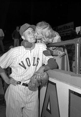 A vintage black-and-white photo of a woman kissing a baseball player in a "VOLS" jersey over a dugout railing.