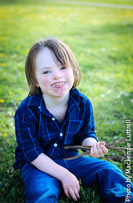 Boy sits in grass holding sticks.