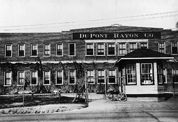 early twentieth century factory building has a bicycle out front next to a guardhouse entry.