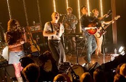 Rock band is playing and singing on a stage lit in warm light.