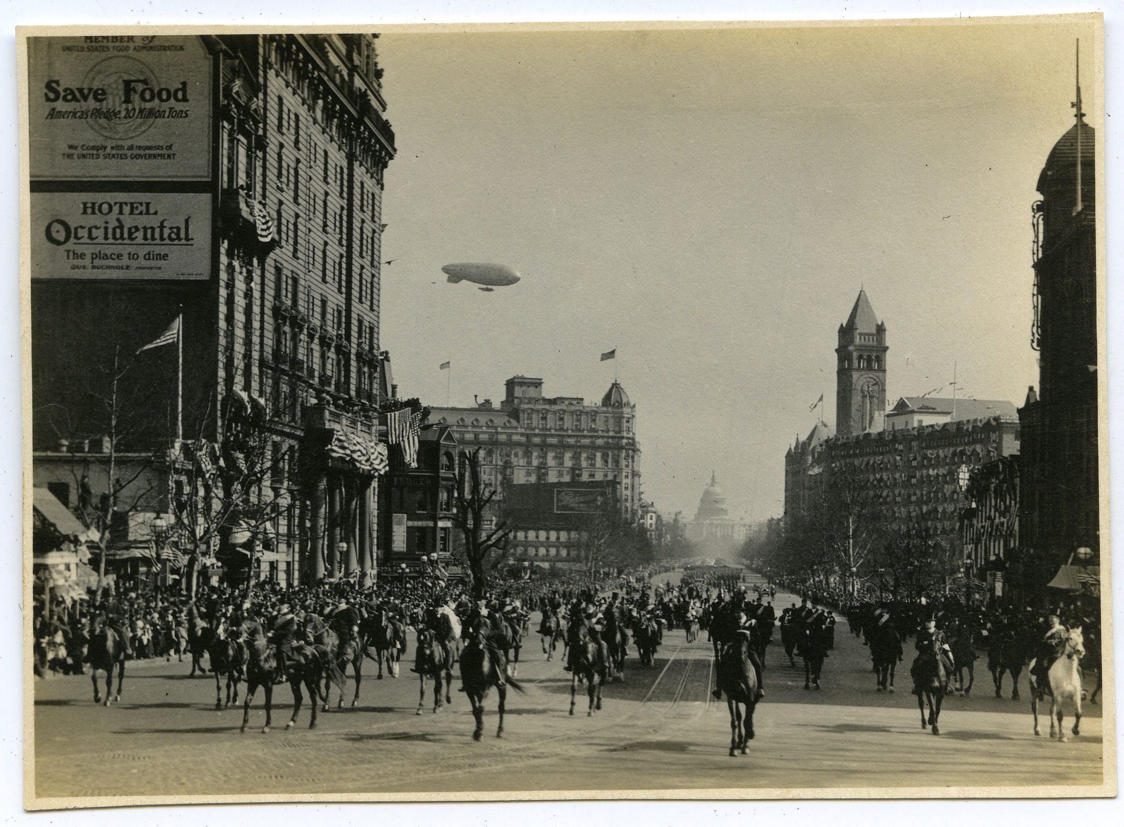 wide avenue in big city. A parade with flags horses and a blimp.