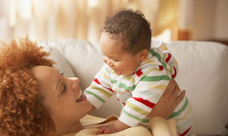 woman holds baby aloft. Both are smiling.