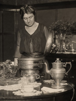 Woman in a kitchen surrounded by old silver.