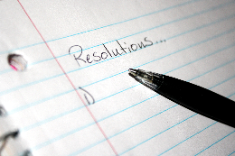 An ink pen hovers over a piece of paper where the word Resolutions is written.