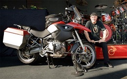 Man in black sits next to a parked motorcycle.