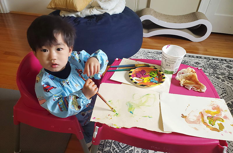 Young boy with dark hair sits at a table and paints.