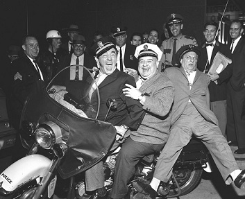 Three men dance around police vehicles.