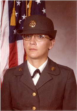 A vintage formal military portrait of a woman in a U.S. Army uniform and hat, standing before an American flag.