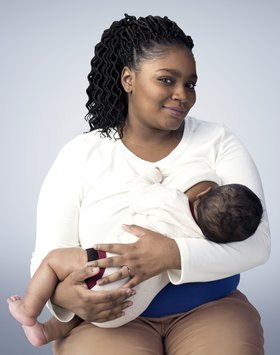 Woman with dark hair and a white shirt breastfeeds her baby.