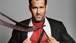 Ryan Reynolds pulls open his white dress shirt and black suit to reveal the red Deadpool superhero costume underneath.
