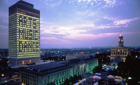 Aerial cityscape with sunset. A skyscraper's windows are lit up to show the words "Arts Music Dance". 