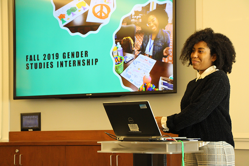 A woman giving a presentation titled "Fall 2019 Gender Studies Internship".
