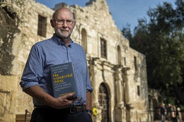 Man in a blue shirt stands in front of the Alamo.