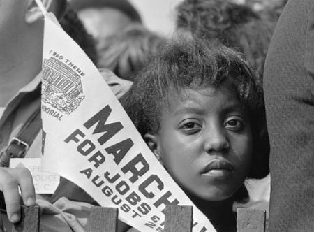 B&W photo of a young girl with a "March for Jobs & Freedom" pennant at the 1963 March on Washington for Civil Rights.