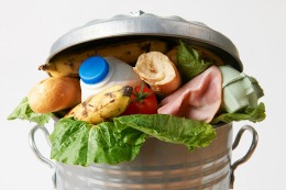Metal trash can with compostable and recyclable materials spilling out.