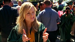 Young blonde woman giving wink and two thumbs up in crowd of people.