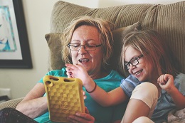 Woman and girl sitting on sofa using tablet computer.