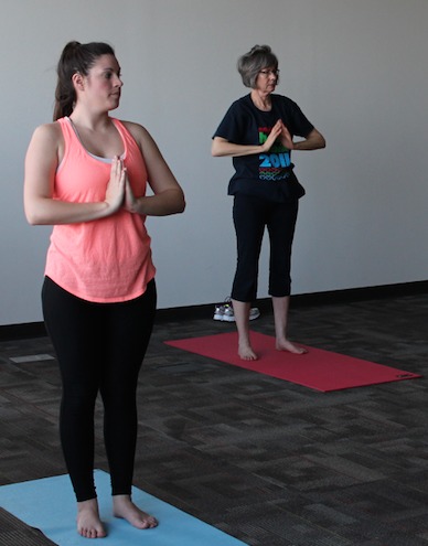 Two people doing standing yoga pose, one on red mat and one on blue mat.