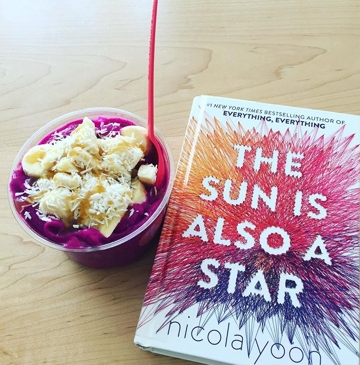The Sun is Also a Star book on table next to a pink dessert with spoon sticking out of bowl.