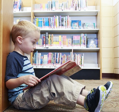 Young blonde boy reading in library.