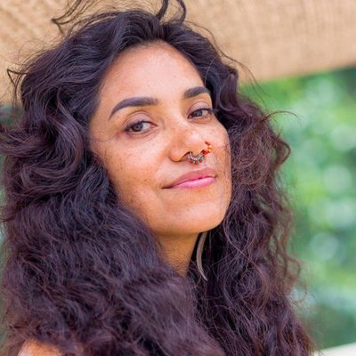 Slightly smiling woman with dark brown wavy hair looking sideways at viewer.