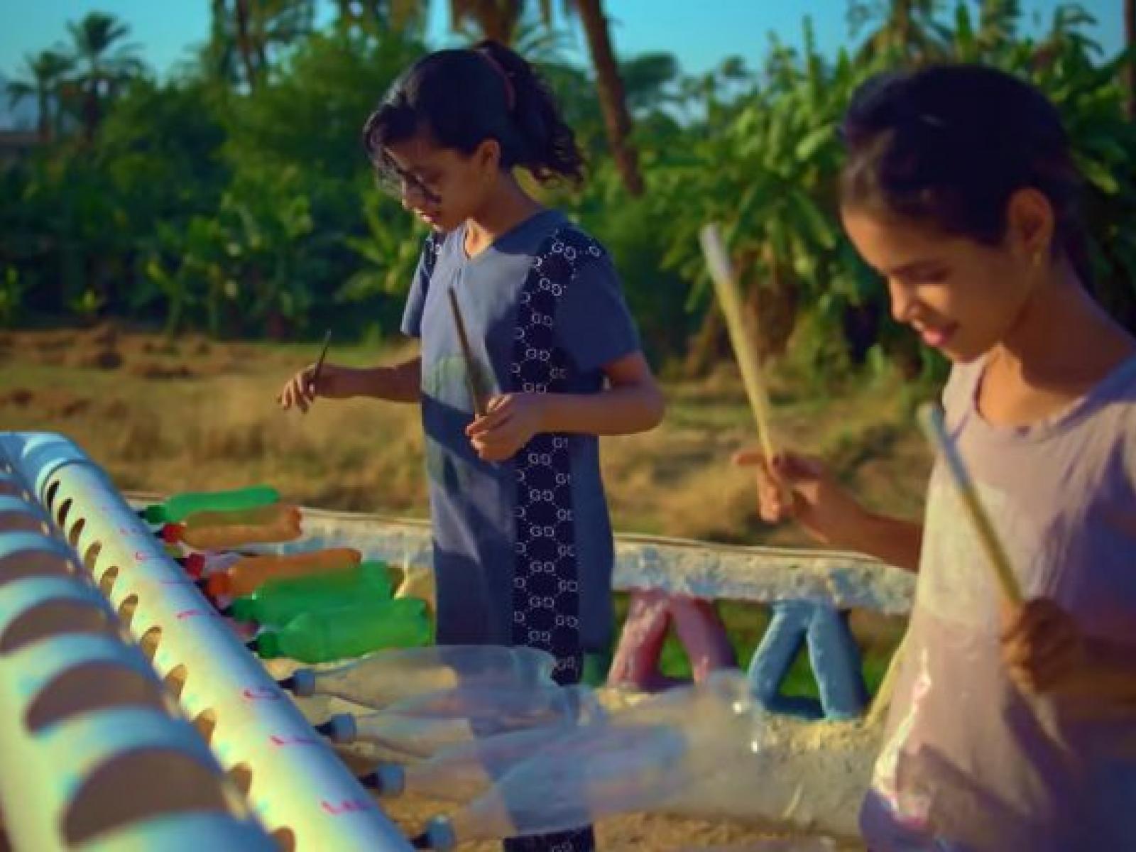 Two children playing a homemade instrument made from old plastic beverage bottles.