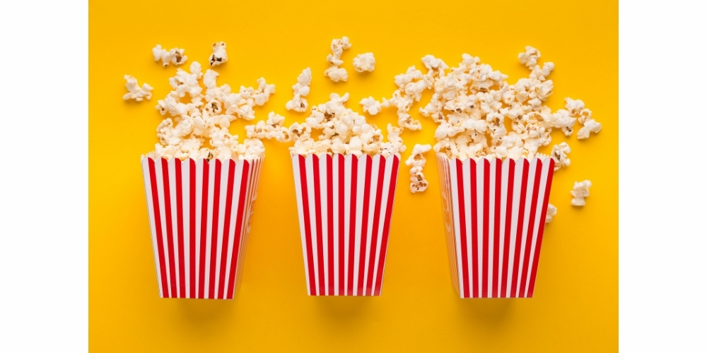Three red and white stripe containers filled with popcorn on a yellow background.