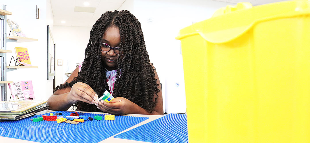 A young girl sits at a LEGO table building something.
