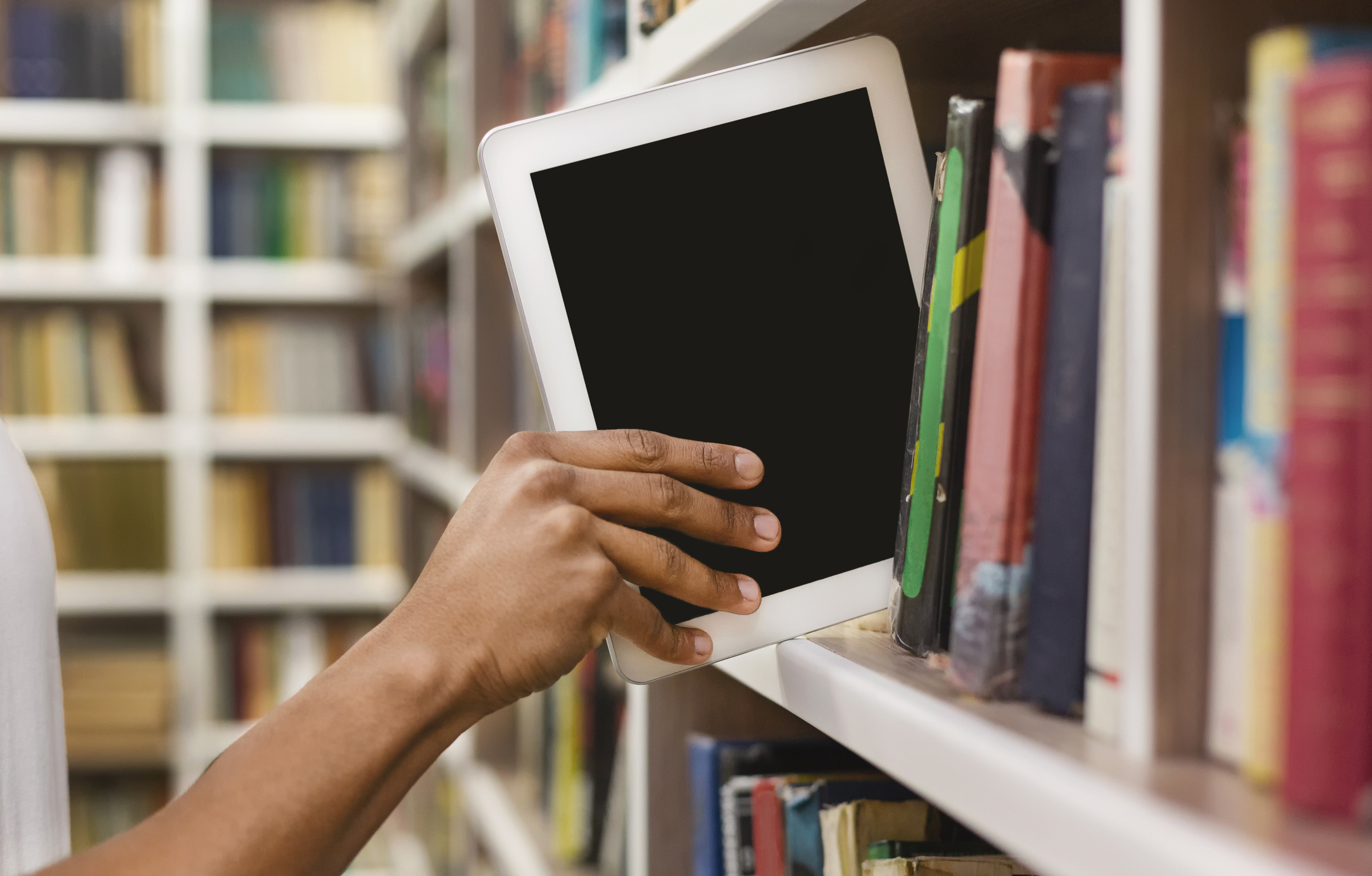 Hand placing an electronic tablet on a bookshelf. 